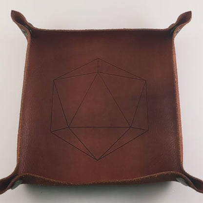 The video starts with a brown leather dice tray in view that has a d20 shape lasered into it. A hand appears from the bottom right corner holding up 10 dark green and black dagger shaped d6s that have red numbers to the camera. The hand rolls the dice into the dice tray from the right.