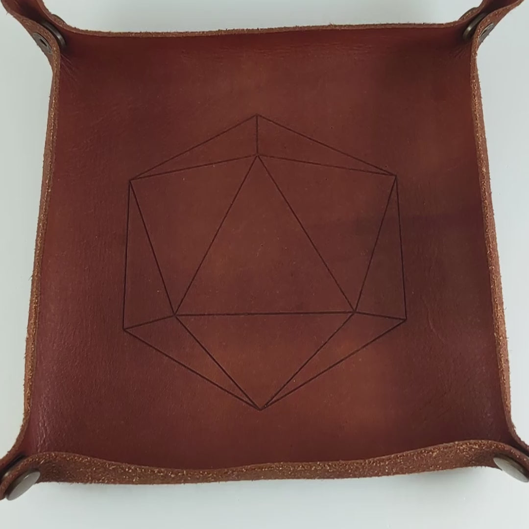 The video starts with a brown leather dice tray in view that has a d20 shape lasered into it. A hand appears from the bottom right corner holding a complete set of dagger dice that are oceanic shades of blue and green with sandy white numbers. The hand rolls all of the dice into the tray from the right.