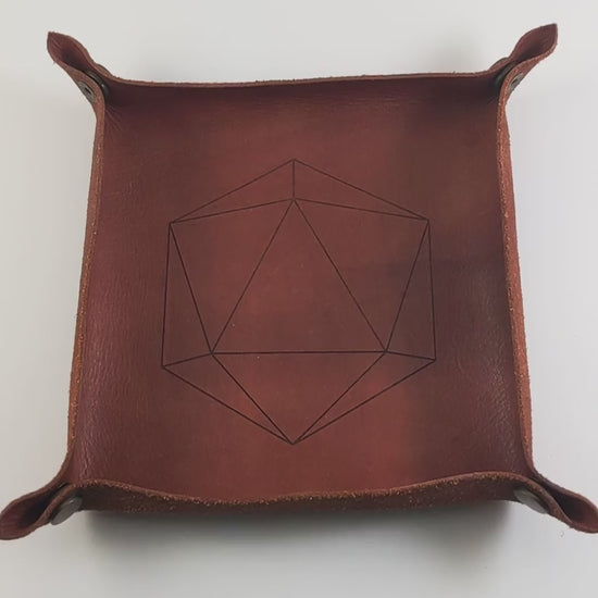 The video starts with a brown leather dice tray in view that has a d20 shape lasered into it. A hand appears from the bottom holding a complete set of emerald green polyhedral dice except for the crystal d4 with gold numbers. The hand rolls all of the dice into the tray from the right.