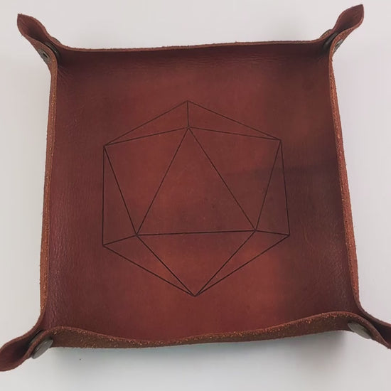 The video starts with a brown leather dice tray in view that has a d20 shape lasered into it. A hand enters from the bottom right corner holding a dark green and black reliable talent d20 with red numbers. The hand spins the d20 to show off how each face that is normally 9 or below is replaced with a 10. Then the hand rolls the die into the tray from the right.