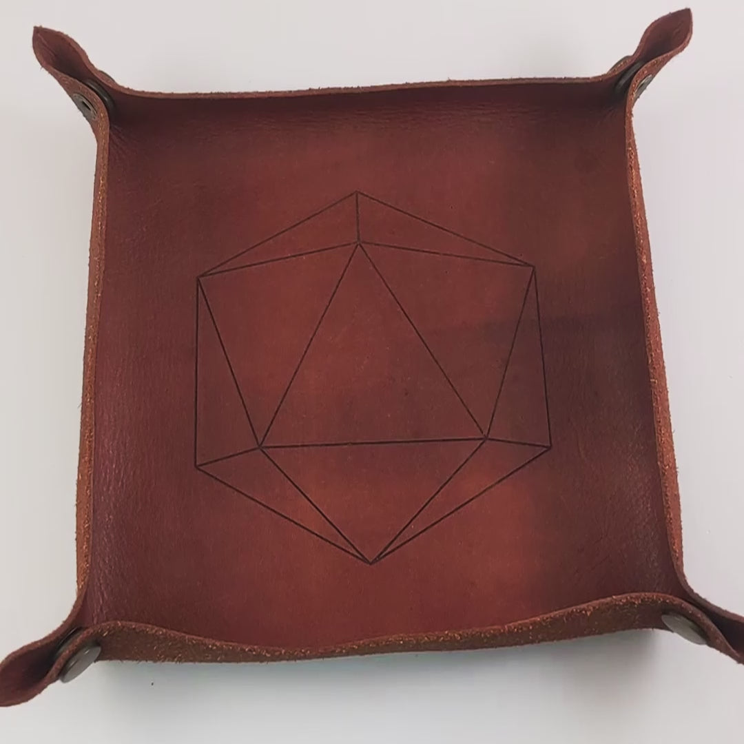 The video starts with a brown leather dice tray in view that has a d20 shape lasered into it. A hand enters from the bottom right corner holding a dark green and black reliable talent d20 with red numbers. The hand spins the d20 to show off how each face that is normally 9 or below is replaced with a 10. Then the hand rolls the die into the tray from the right.