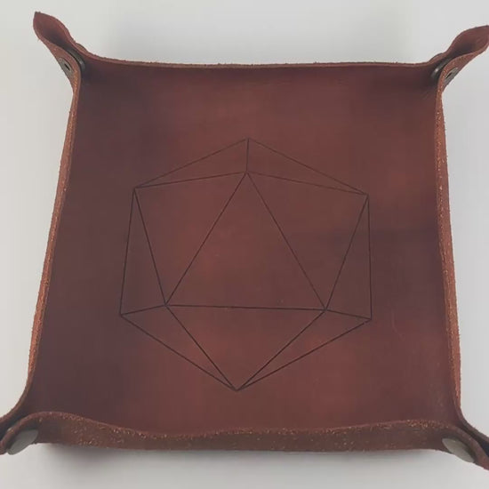 The video starts with a brown leather dice tray in view that has a d20 shape lasered into it. A hand appears from the bottom right corner holding a complete set of dagger dice that are black with crimson red splatters with silver numbers. The hand rolls all of the dice into the tray from the right.