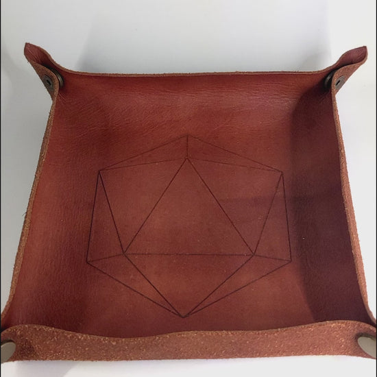 The video starts with a brown leather dice tray in view that has a d20 shape lasered into it. A hand appears from the bottom right corner holding a complete set of polyhedral dice that are purple, pink, and blue swirls with a clear shell with extra glitter and white numbers. The hand rolls all of the dice into the tray from the right.